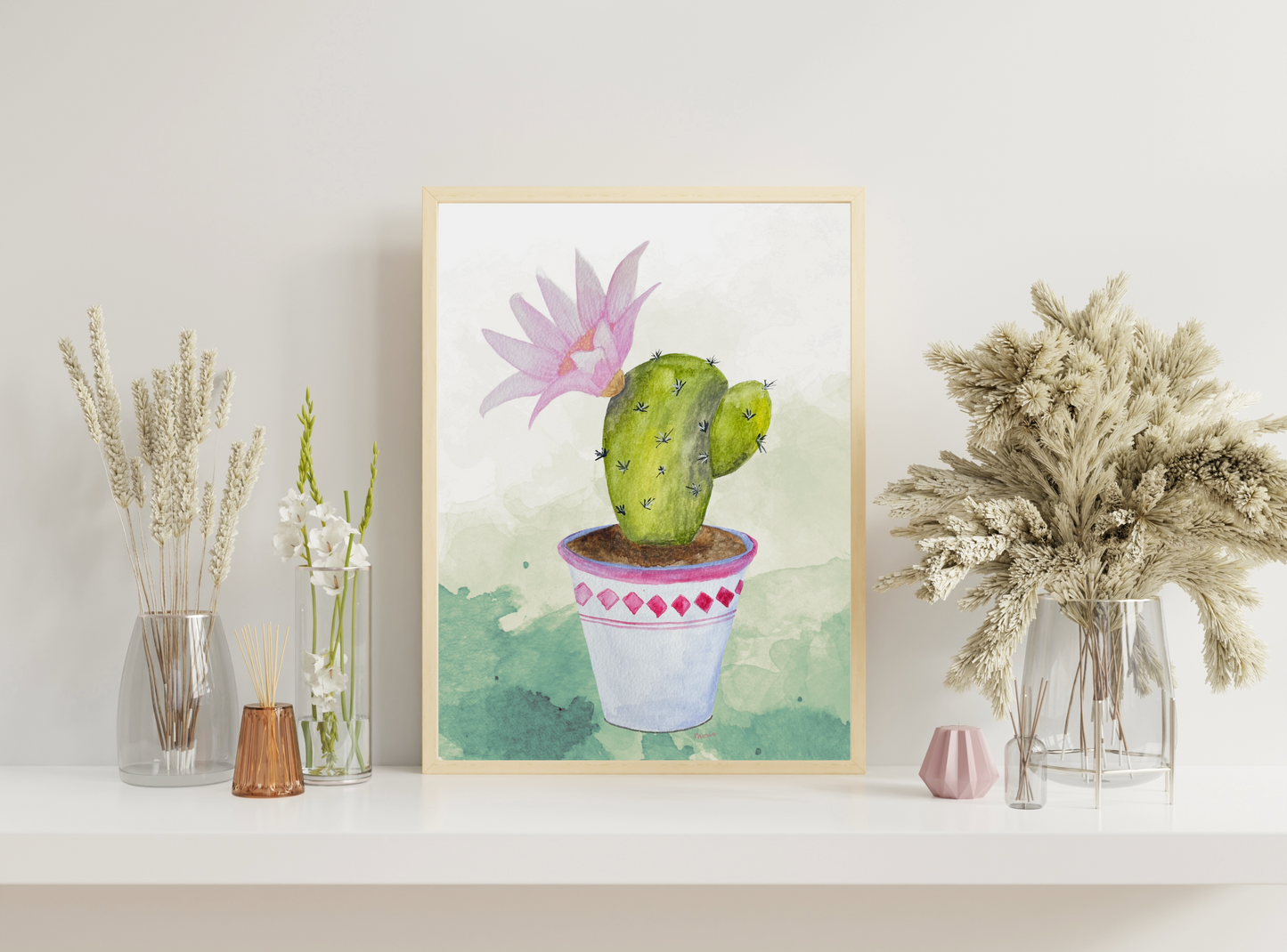 Framed artwork of a cactus with a pink flower on a shelf with decorative plants.