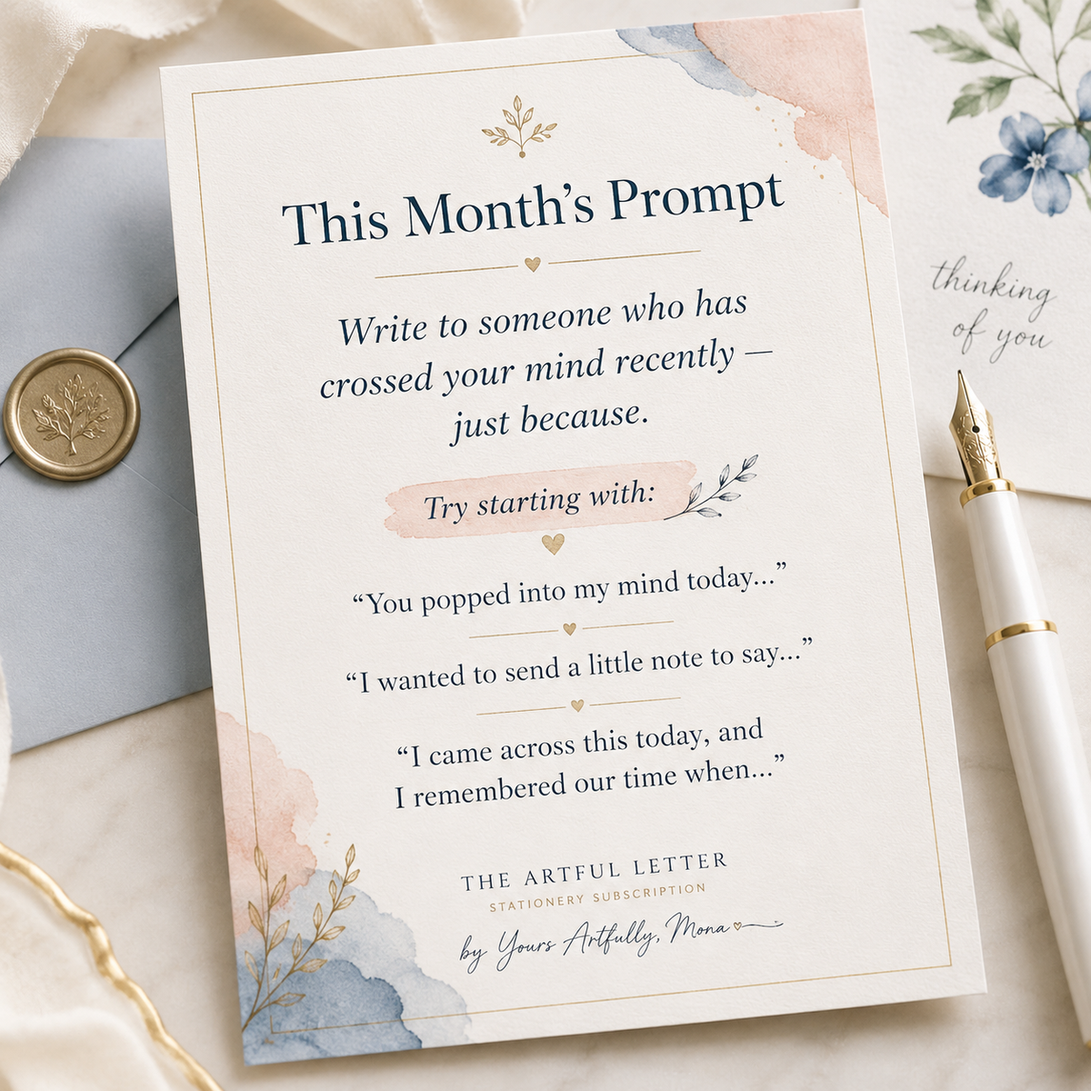 A stationery card titled 'This Month's Prompt' with watercolor floral accents, styled on a marble surface with a blue envelope, gold wax seal, and white pen.