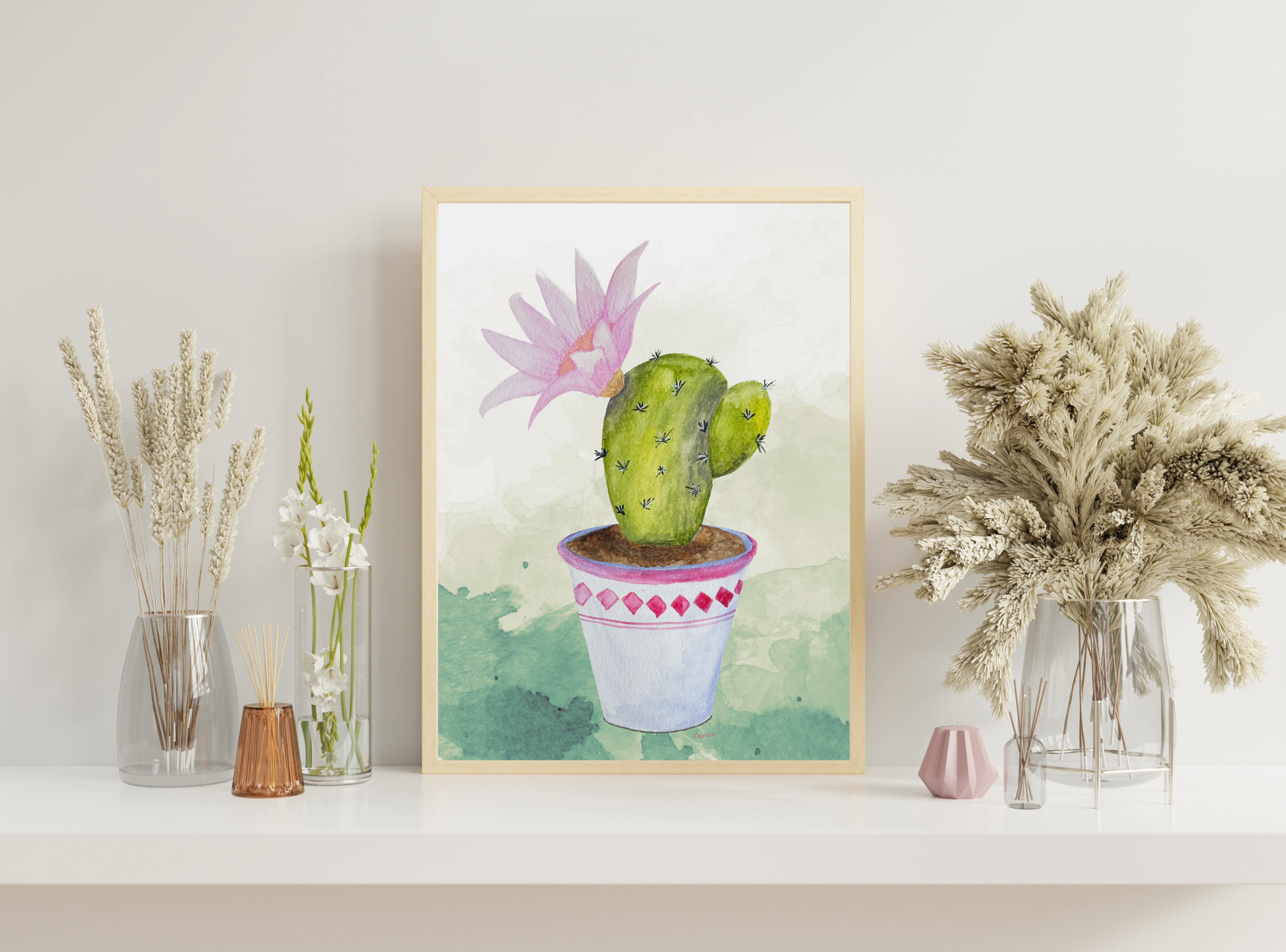 Framed artwork of a cactus with a pink flower on a shelf with decorative plants.
