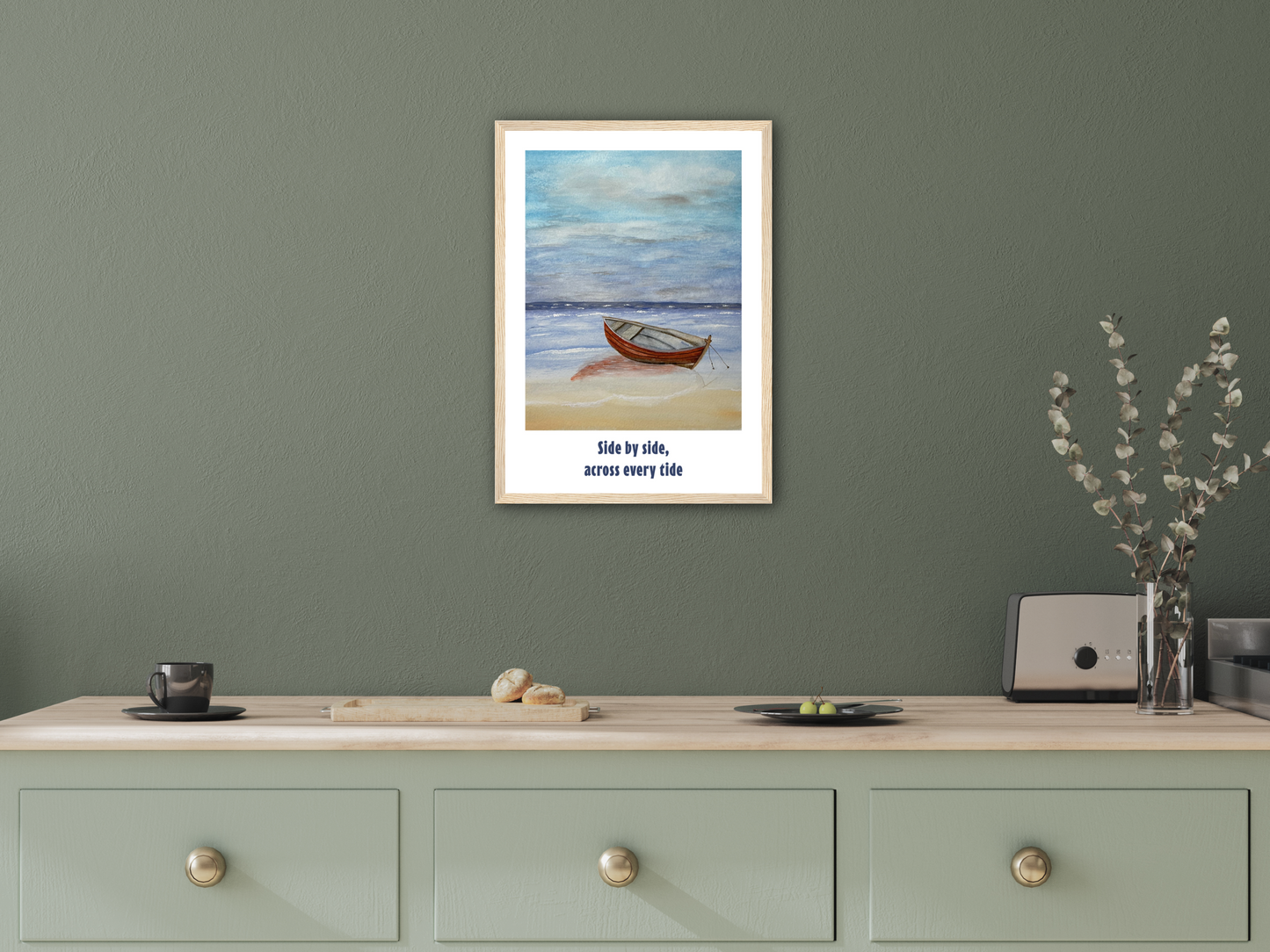 A framed art print featuring a small wooden boat on a beach with the text 'Side by side, across every side' displayed on a light wood console table against a sage green wall.