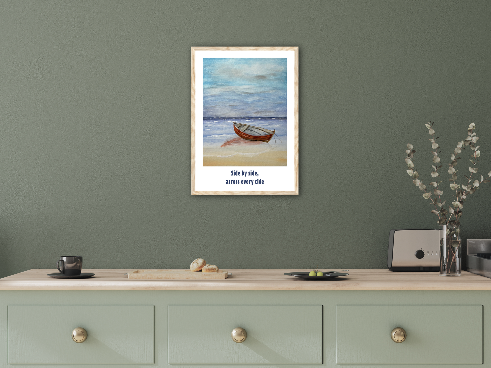 A framed art print featuring a small wooden boat on a beach with the text 'Side by side, across every side' displayed on a light wood console table against a sage green wall.