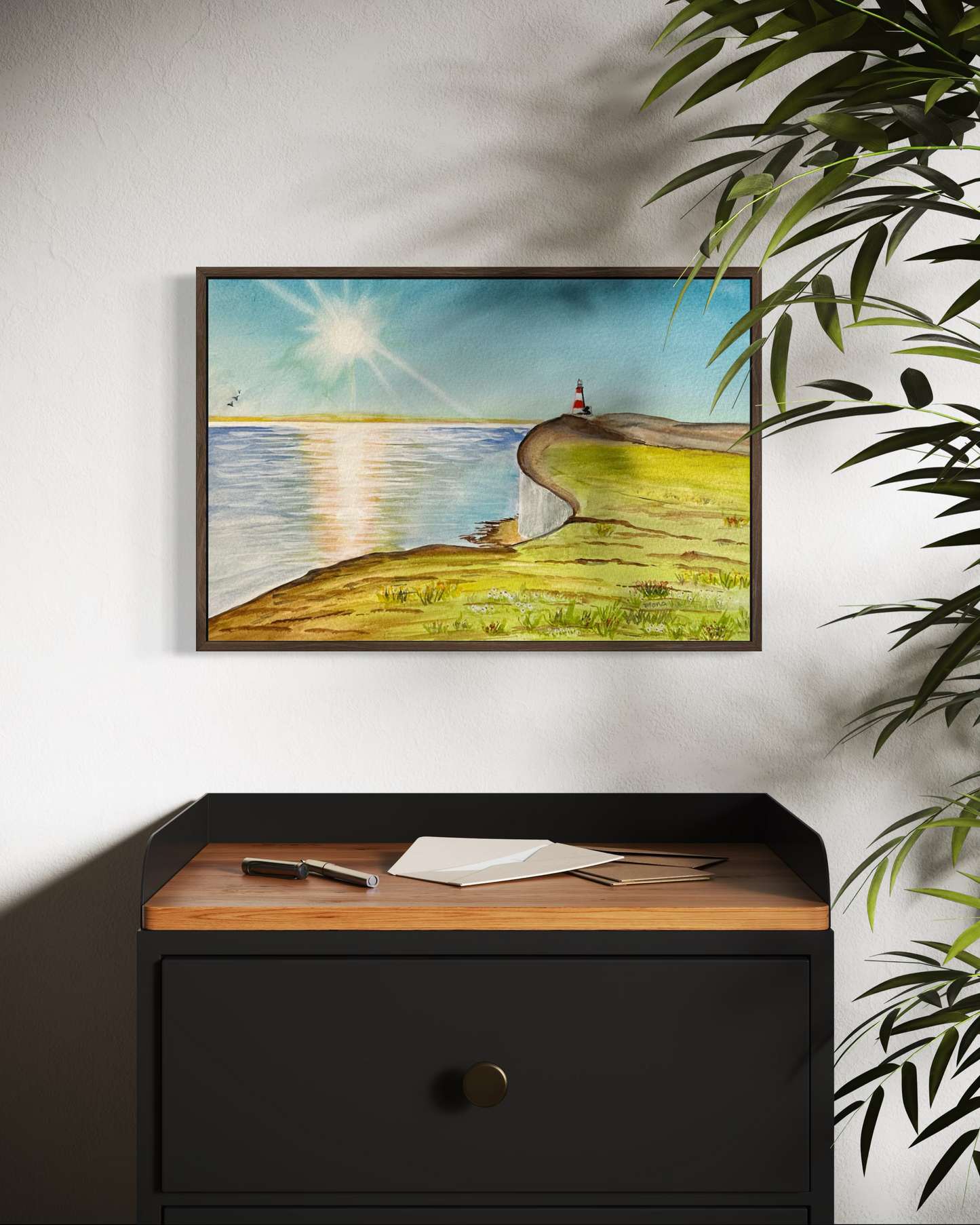 Framed artwork of a person walking along a path by a lake on a wall above a black cabinet with wooden top.