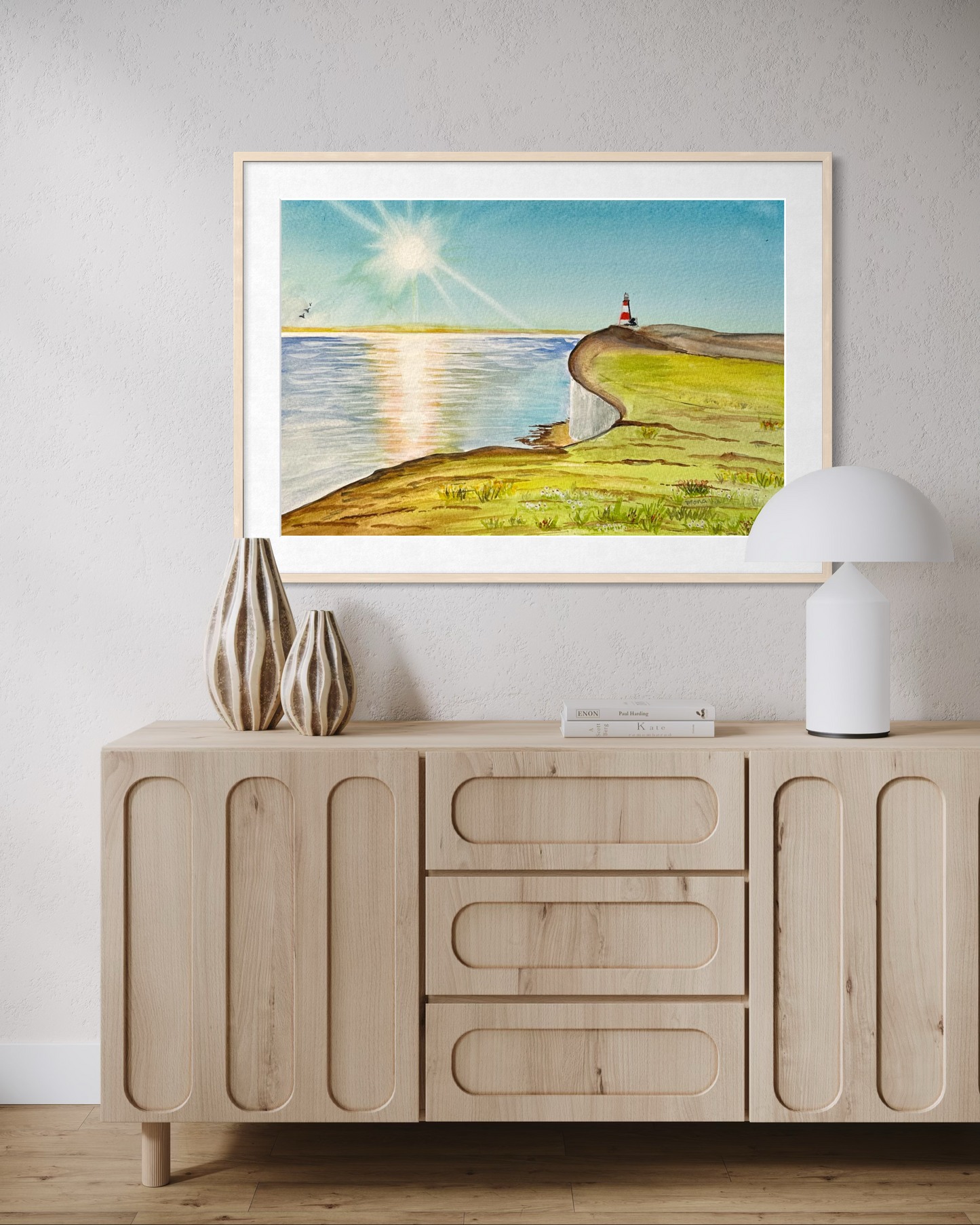 Framed artwork of a coastal scene above a wooden sideboard with decorative items.